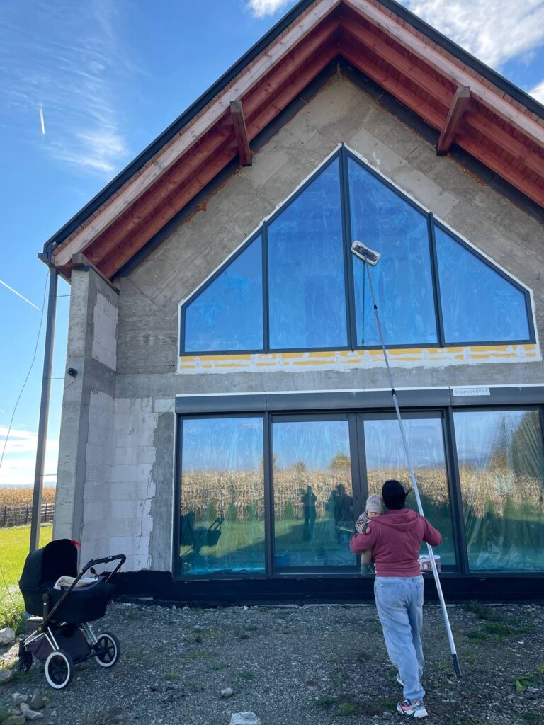 Mycie dużych okien w domu mikrowłóknami na długim kiju z dzieckiem w ręku